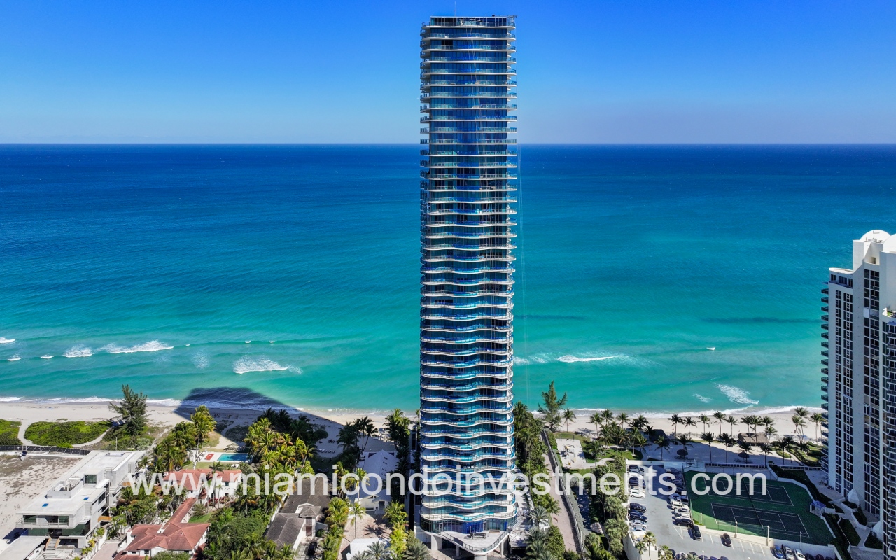Ragalia drone view facing condo building front exterior with blue ocean backdrop