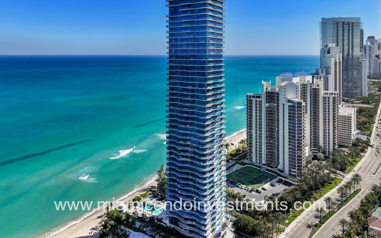 Ragalia drone view closeup facing condo building exterior side angle with blue ocean backdrop