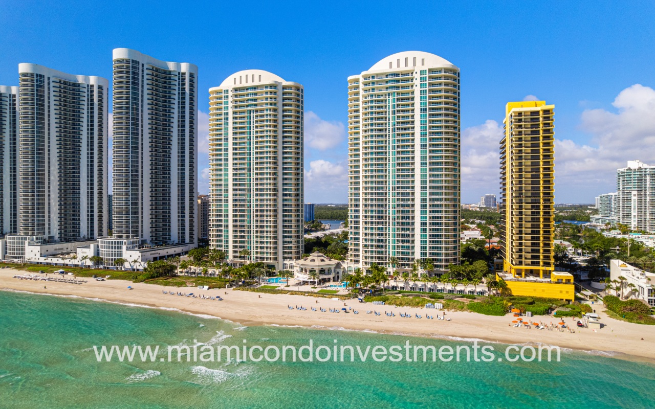 Turnberry Ocean Colony North drone view facing condo buildings and other buildings along ocean shoreline from above ocean