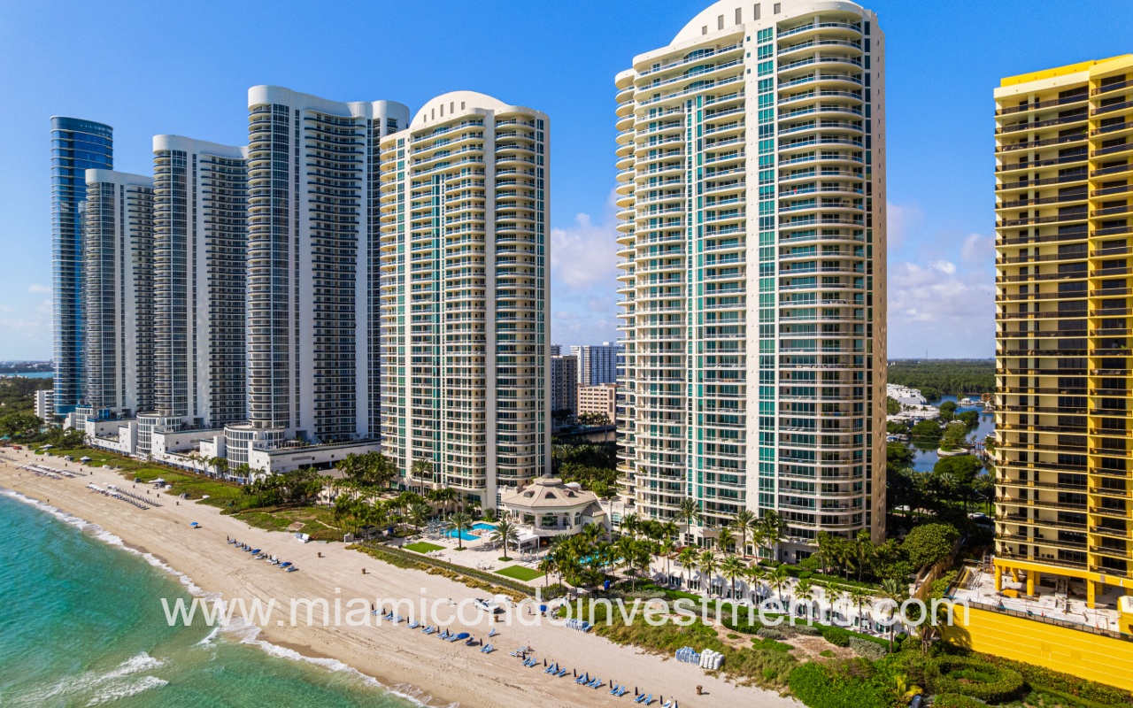 Turnberry Ocean Colony North drone view closeup of condo building and other buildings along ocean shoreline from above ocean