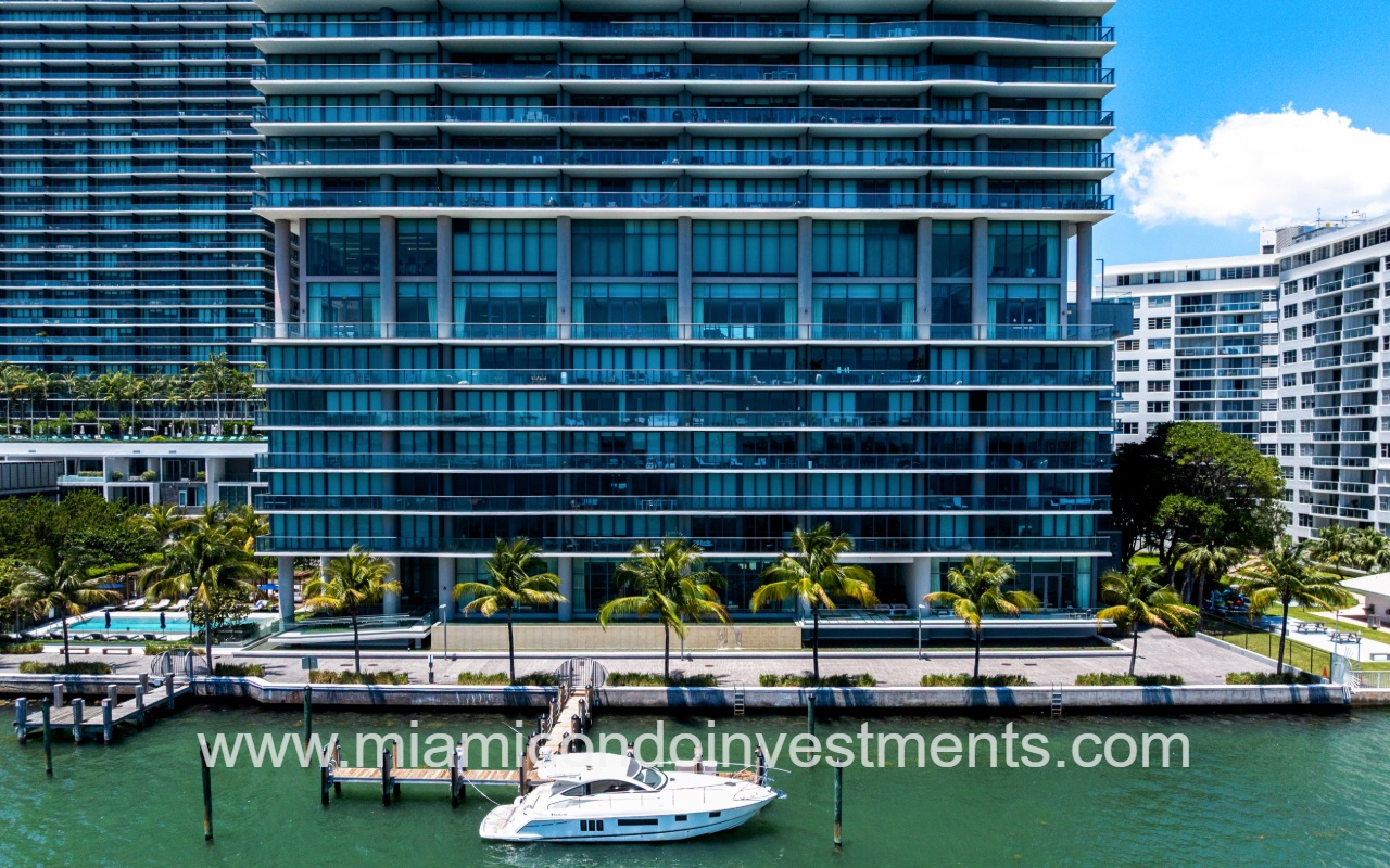 One Paraiso drone directly facing lower condo building exterior with boat docked on the waterfront