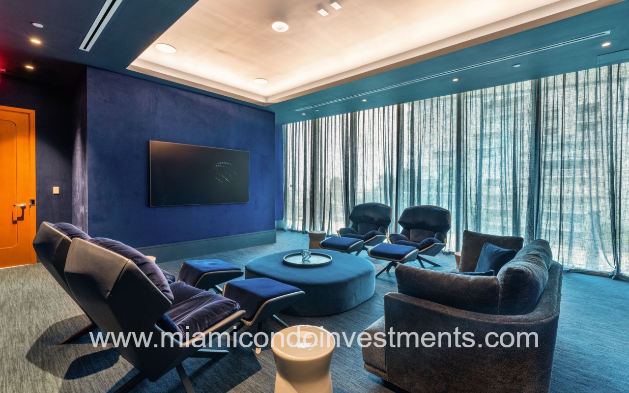 UNA Residences condominium building modern blue-toned movie theater with curved seating around a circular ottoman and large windows with sheer curtains.