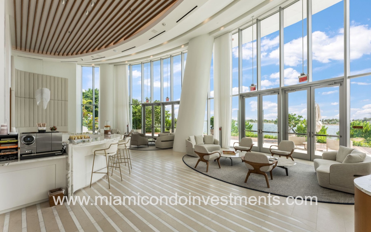 UNA Residences condominium building right modern lounge with curved white seating, a marble bar, and floor-to-ceiling windows overlooking water