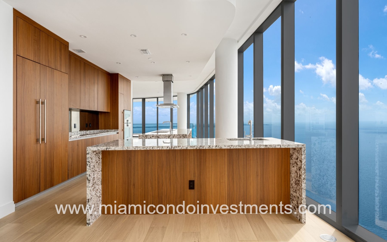 UNS Residences condominium building 4-bedroom open-concept kitchen with wood cabinets, granite island, and large floor-to-ceiling windows overlooking Biscayne Bay