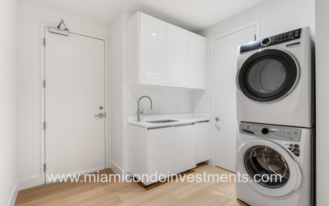 UNA Residences condominium building laundry room with stacked front-loading washer and dryer, white cabinets, and a sink with modern faucet