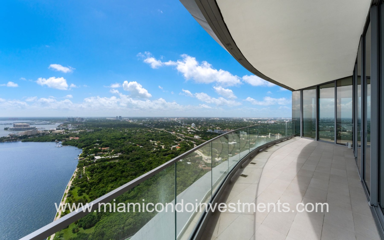 UNA Residences condominium building curved balcony with glass railing overlooking Biscayne bay and green landscape, on a sunny day