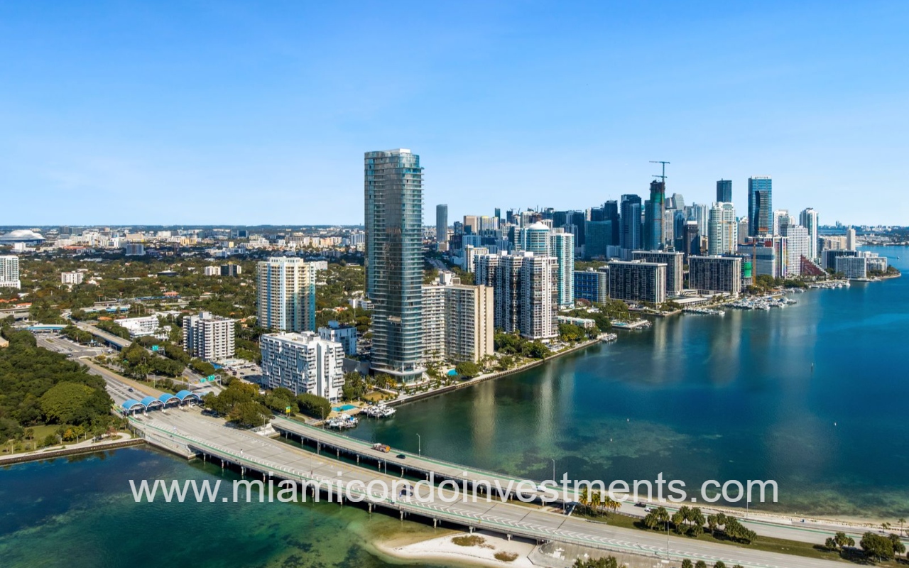 UNA Residences aerial view condominium building and skyscrapers along Biscayne Bay with Rickenbacker Causeway crossing the water at foreground.